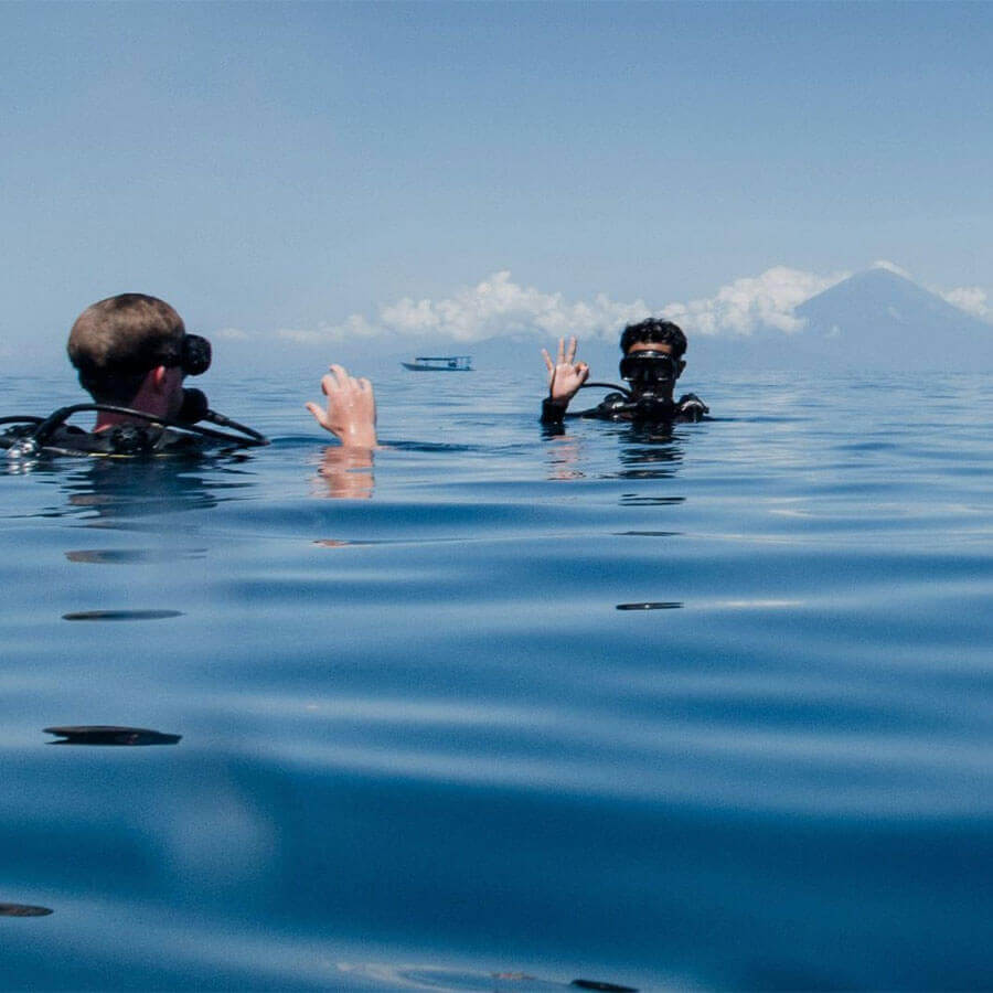 Two people in scuba gear in the ocean with a mountain in the background.