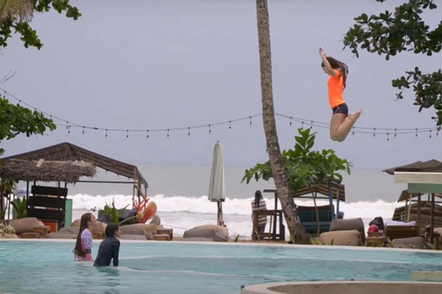 A young girl jumping into the pool at a resort.