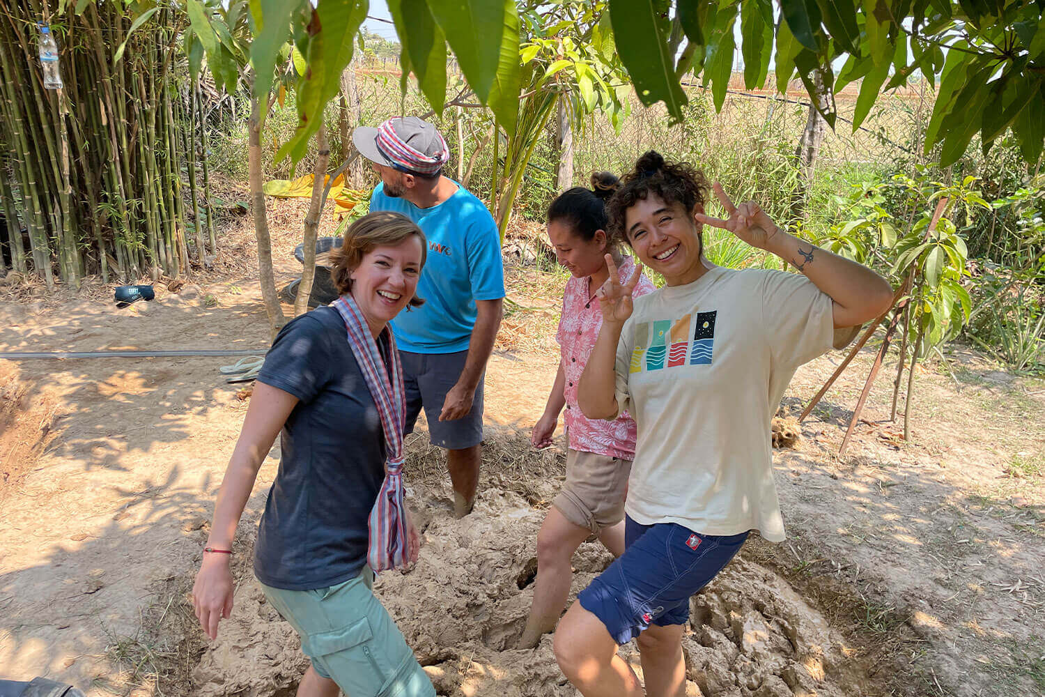 Four people are standing in mud with a tree.